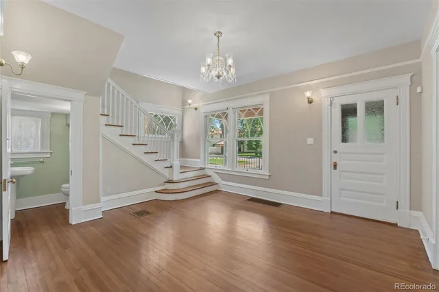 an empty room with wooden floor chandelier and windows