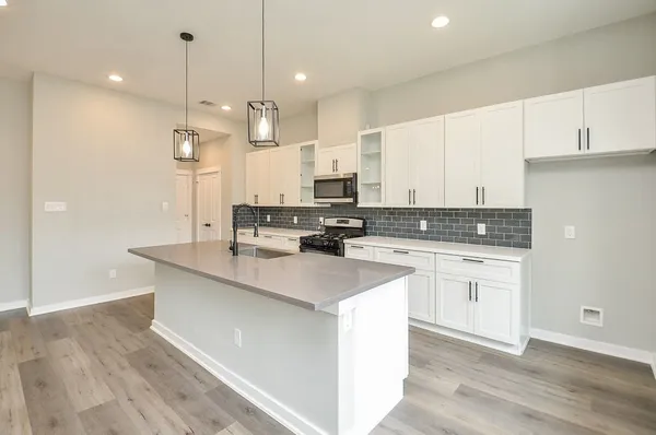 a large kitchen with stainless steel appliances kitchen island granite countertop a stove a sink a refrigerator and white cabinets with wooden floor