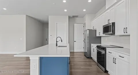 a kitchen with stainless steel appliances a stove top oven a sink a refrigerator white cabinets and wooden floor