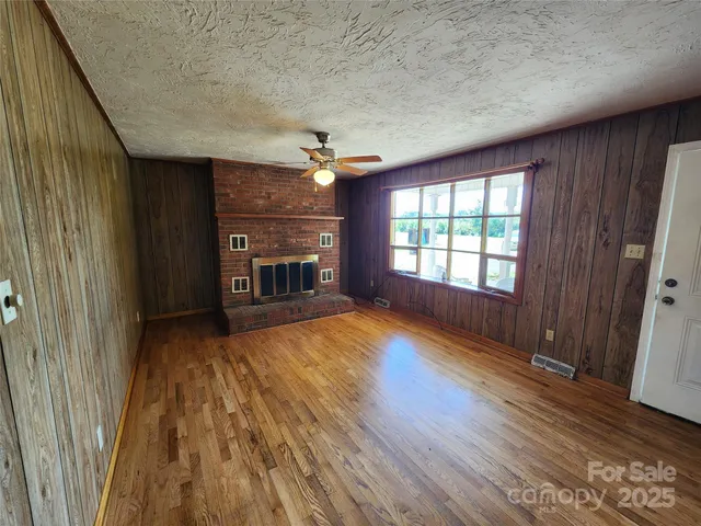 an empty room with wooden floor fireplace and windows