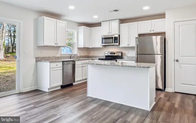 a kitchen with stainless steel appliances granite countertop a stove top oven a refrigerator a sink and white cabinets with wooden floor