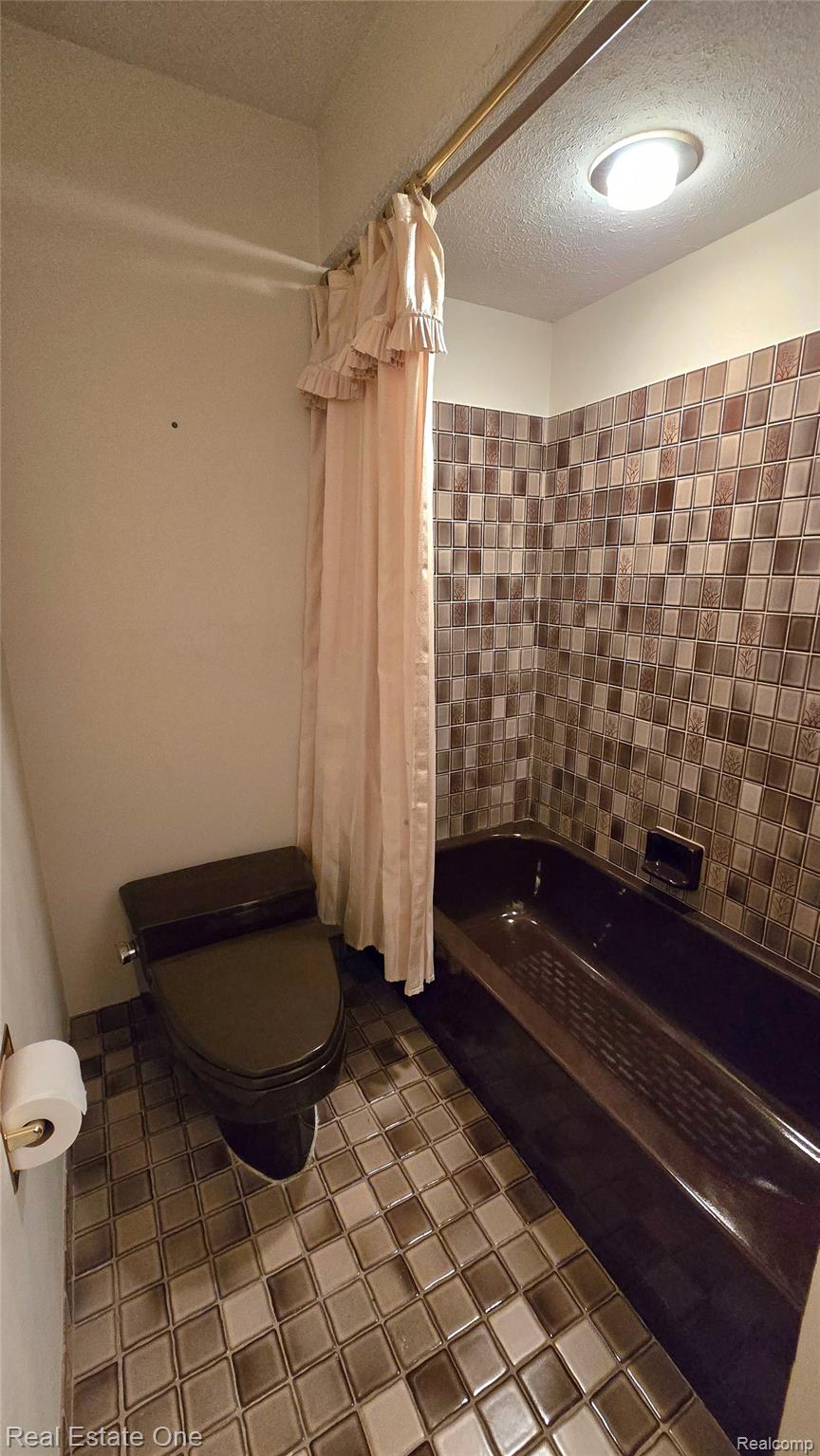 8950 Wise Road Commerce Township, MI 48382 - Photo 16 of 39 Bathroom featuring a built-in tub, dark-toned toilet, and a tiled floor with a diamond pattern