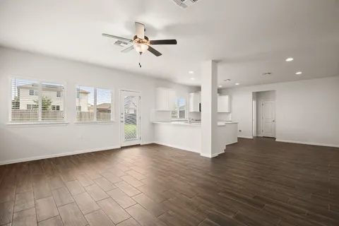 a view of an empty room with wooden floor and a kitchen