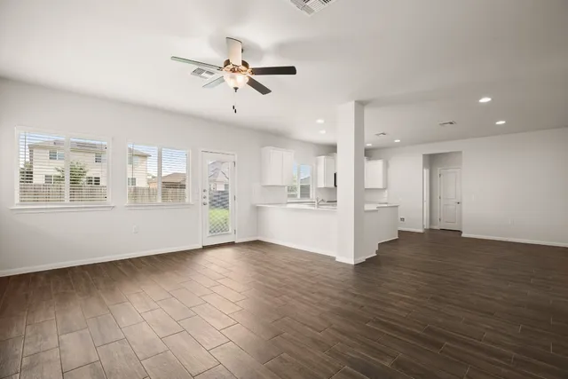 a view of an empty room with wooden floor and a kitchen