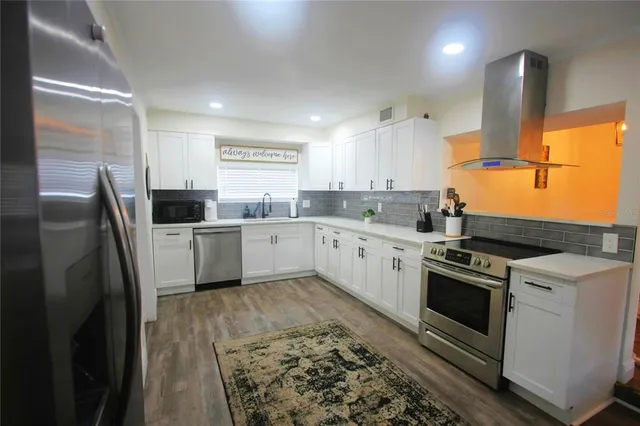 a kitchen with stainless steel appliances granite countertop a sink a stove a refrigerator and island with wooden floor