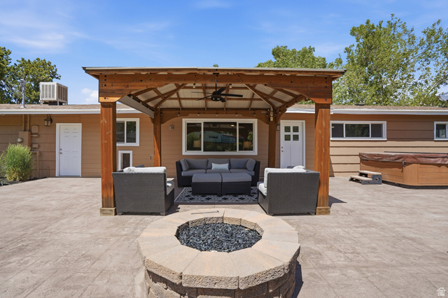 6889 South Village Road Salt Lake City, UT 84121 - Photo 28 of 44 Expansive hardscaped patio featuring a substantial wood pergola with a ceiling fan, a built-in stone fire pit, and a separate hot tub