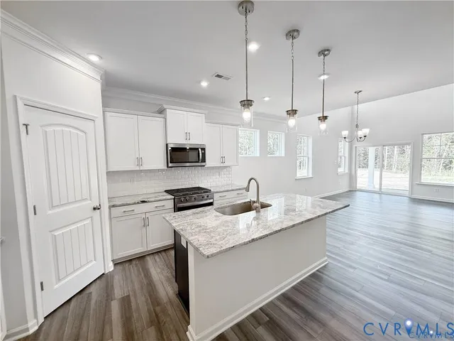 a kitchen with stainless steel appliances granite countertop a sink a stove a refrigerator and white cabinets with wooden floor