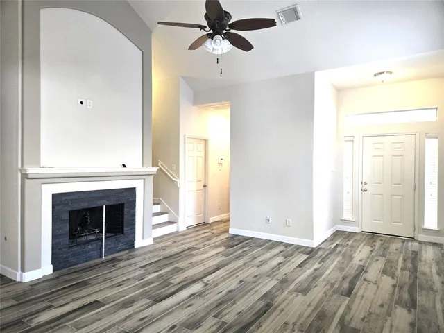 an empty room with wooden floor a ceiling fan and a fireplace