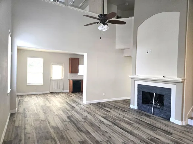 an empty room with wooden floor a ceiling fan a fireplace and windows