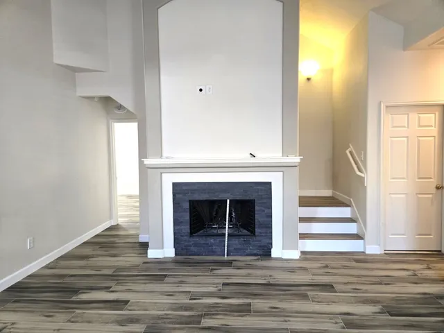 a view of an empty room with wooden floor and a fireplace