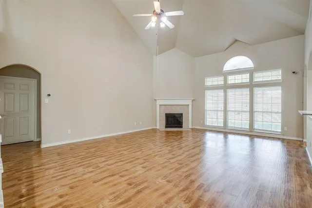 an empty room with wooden floor chandelier fan and windows
