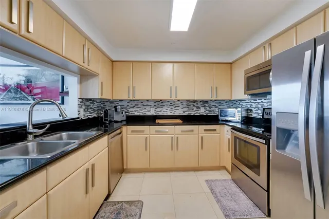 a kitchen with granite countertop stainless steel appliances a sink dishwasher a refrigerator oven and white cabinets