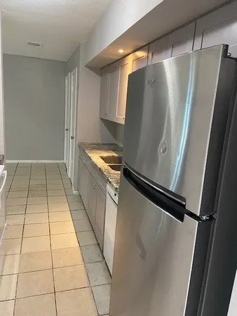 a view of a refrigerator in kitchen and an empty room in wooden floor