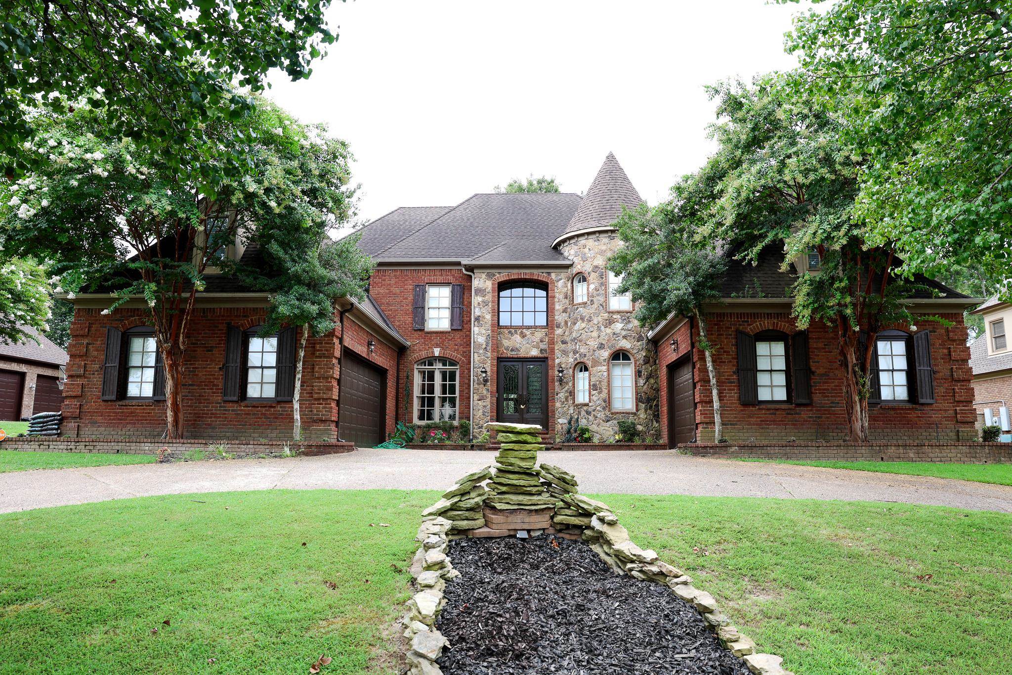 French country home with a front yard, a garage, brick siding, roof with shingles, and driveway