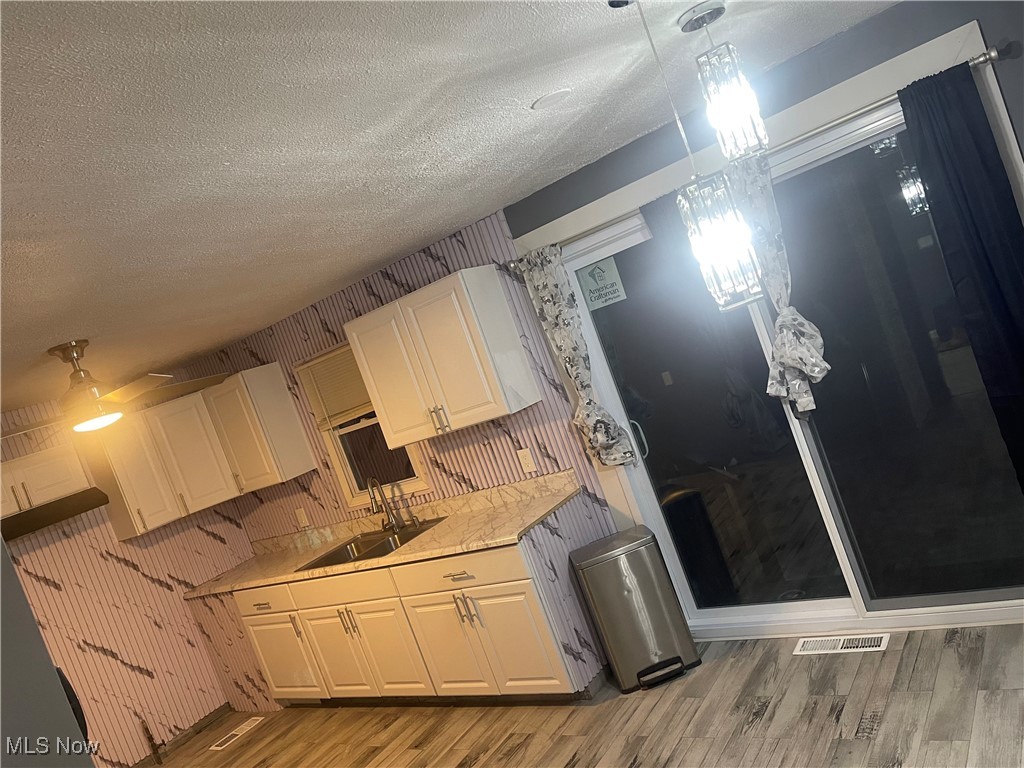603 Liberty Road Youngstown, OH 44505 - Photo 10 of 42 Kitchen with light countertops, white cabinets, hanging light fixtures, light wood-type flooring, and a textured ceiling