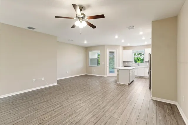 a view of a big room with wooden floor a ceiling fan and windows