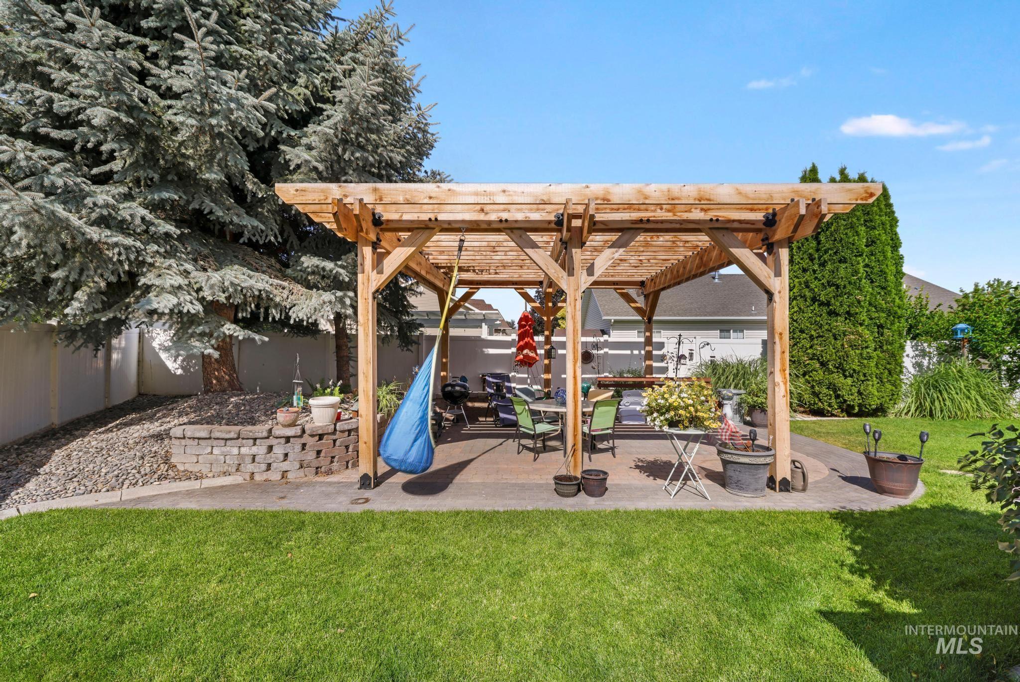 467 Wildrose Loop Twin Falls, ID 83301 - Photo 38 of 46 Expansive backyard featuring a natural wood pergola over a concrete patio, a retaining wall with rock landscaping, a manicured lawn, and mature evergreen trees