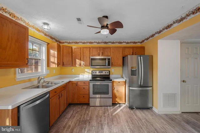 a kitchen with stainless steel appliances granite countertop a refrigerator a sink dishwasher a stove and white countertops with wooden floor