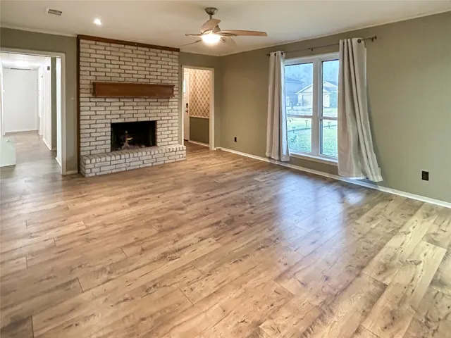 an empty room with wooden floor fireplace and windows