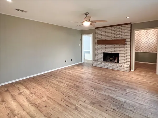 a view of an empty room with wooden floor fireplace and a window