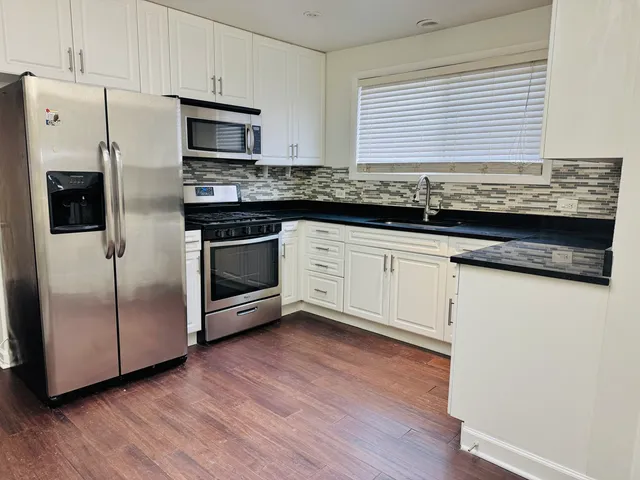 a kitchen with granite countertop wooden floors stainless steel appliances and sink