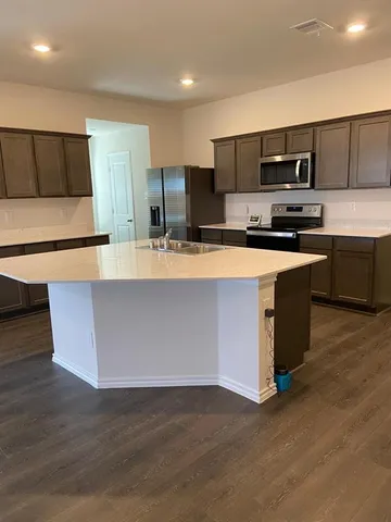 a large kitchen with stainless steel appliances a large counter top a stove a microwave a sink and a refrigerator