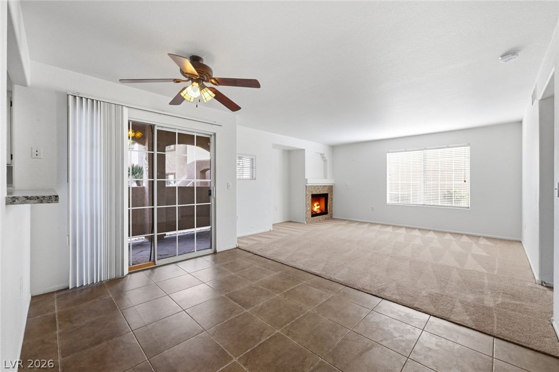 1851 Hillpointe Road, Unit 1311 Henderson, NV 89074 - Photo 18 of 47 Unfurnished living room with a ceiling fan, light carpet, a warm lit fireplace, and light tile patterned floors