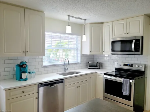 a kitchen with stainless steel appliances granite countertop white cabinets a sink a stove a microwave and wooden floors