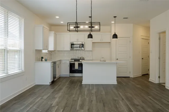 a kitchen with stainless steel appliances granite countertop a white stove top oven a sink dishwasher and a refrigerator with wooden floor