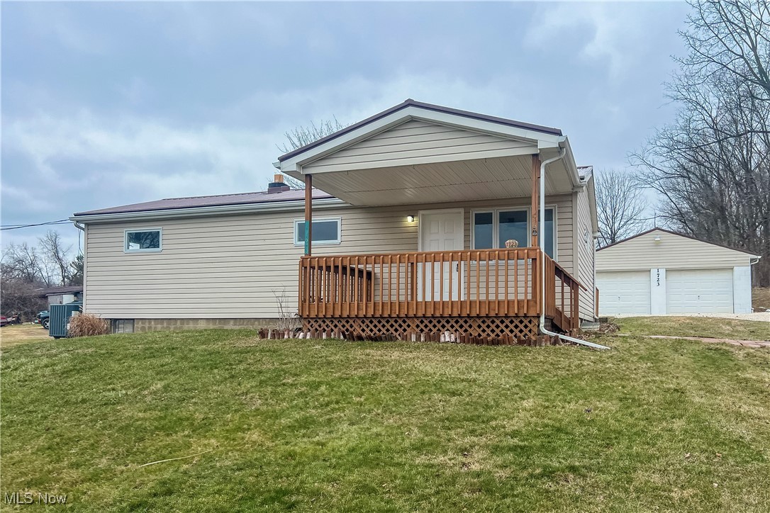 Rear view of property with a garage, a lawn, an outdoor structure, and cooling unit
