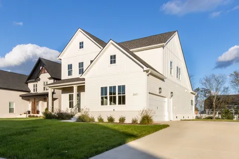 a view of a white house next to a yard with big trees