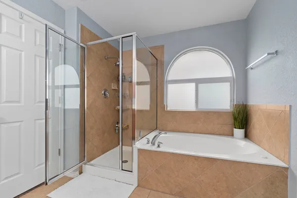 a bathroom with a tub a window and a glass door shower