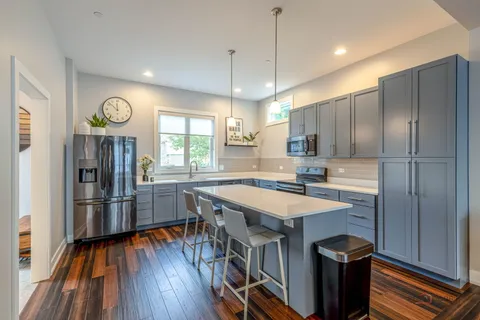 a kitchen with stainless steel appliances granite countertop a refrigerator a sink dishwasher a stove and a dining table with wooden floor