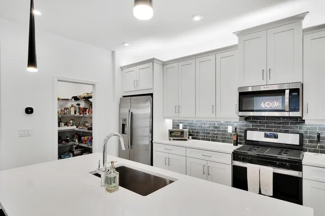 a kitchen with stainless steel appliances a stove a sink a refrigerator and white cabinets with wooden floor