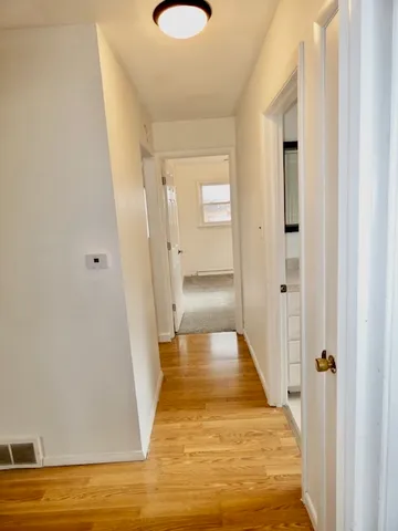 a view of a hallway with wooden floor and a bathroom