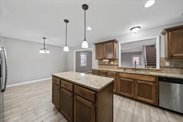 a kitchen with stainless steel appliances granite countertop a stove top oven a sink dishwasher and a refrigerator with wooden floor