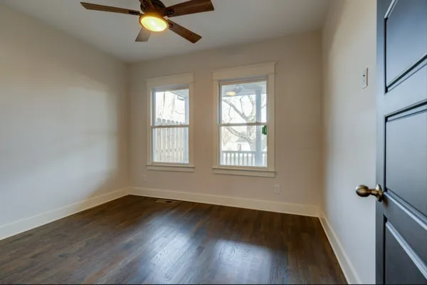 an empty room with wooden floor fan and windows