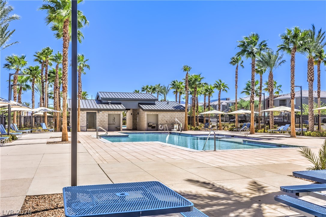 12103 Mojave Gold Road, Unit 4 Las Vegas, NV 89183 - Photo 20 of 23 A sparkling swimming pool surrounded by towering palm trees and stone decking under clear skies.