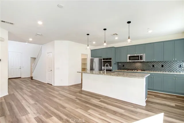 a large white kitchen with stainless steel appliances granite countertop a refrigerator a oven and white cabinets with wooden floor