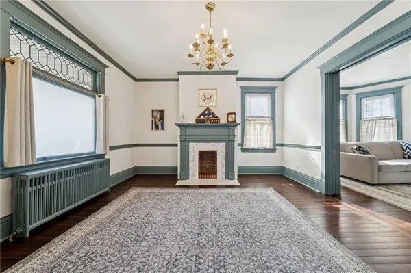 a view of a livingroom with a fireplace a chandelier wooden floor and windows