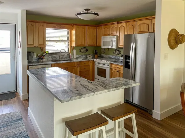 a kitchen with granite countertop a refrigerator a stove a sink cabinets and wooden floor