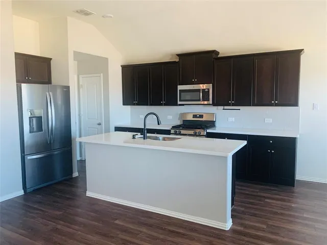 a kitchen with kitchen island a black refrigerator stove top oven and wooden floor