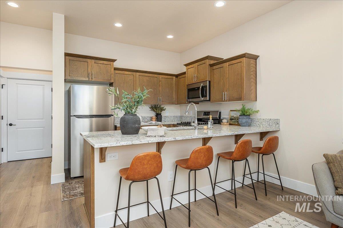1439 North Bluffs Ridge Lane Boise, ID 83704 - Photo 27 of 47 Kitchen with a kitchen breakfast bar, light stone countertops, stainless steel appliances, brown cabinets, and a peninsula