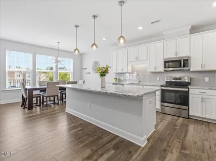 a kitchen with kitchen island granite countertop a stove a sink a dining table and chairs with wooden floor