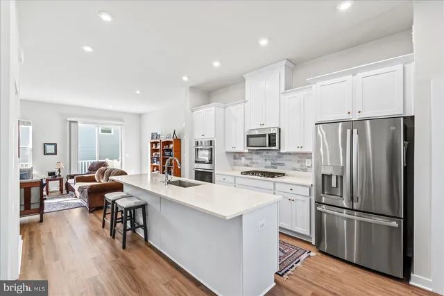 a kitchen with stainless steel appliances kitchen island granite countertop a refrigerator a stove a sink a dining table and chairs with wooden floor