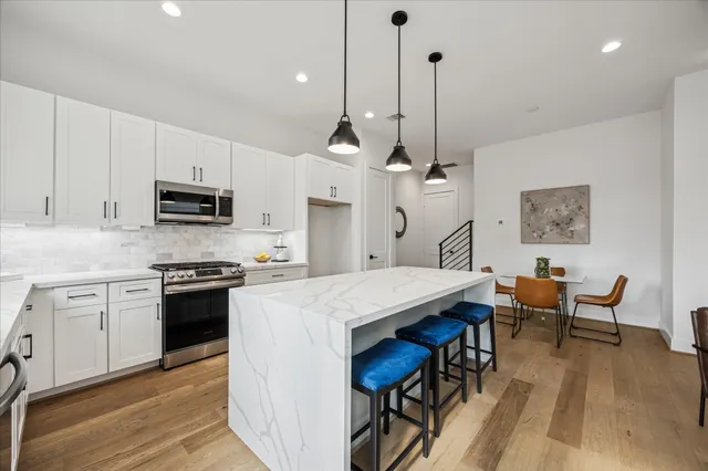 a kitchen with stainless steel appliances granite countertop a stove a sink a dining table and chairs with wooden floor