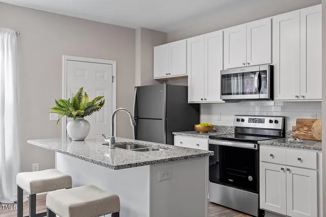 a kitchen with stainless steel appliances granite countertop a refrigerator a sink a stove and white cabinets