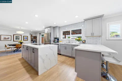 a large white kitchen with a stove a sink a refrigerator and a dining table with wooden floor