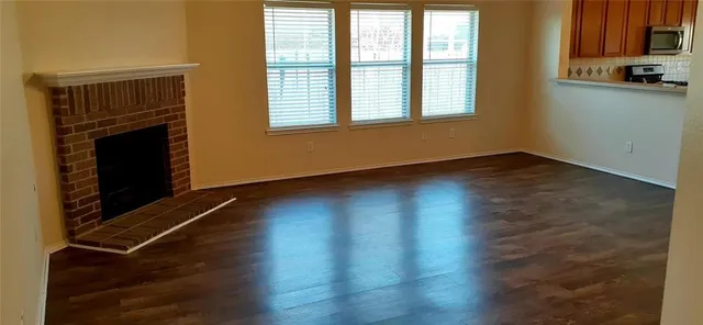 an empty room with wooden floor fireplace and windows