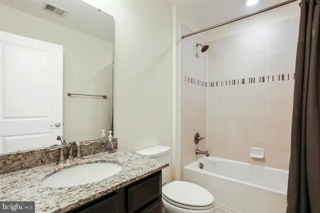 a bathroom with a granite countertop bathtub shower sink vanity mirror and toilet